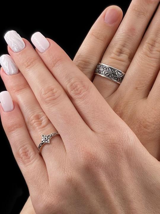 A professional studio photograph of a matching two-piece sterling silver wedding ring set. Both rings feature a prominent, raised Greek-style cross motif in the center, which holds a round, bezel-set white crystal. The interior of the cross arms has a fine, cross-hatched grid texture. Along the sides of the high-polished silver bands are recessed, four-lobed quatrefoil shapes. The rings are presented against a pitch-black background, making the p __etsy:8051335185