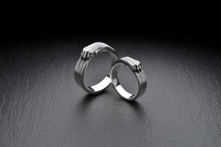 A pair of gothic sterling silver wedding rings featuring sculpted claw details that wrap organically around each band. The dramatic design blends polished metal with textured claw surfaces, creating a symbolic representation of unity and strength. Ideal for alternative couples who appreciate bold artisan jewelry with dark, meaningful aesthetics and handcrafted quality suitable for weddings or promise rings.