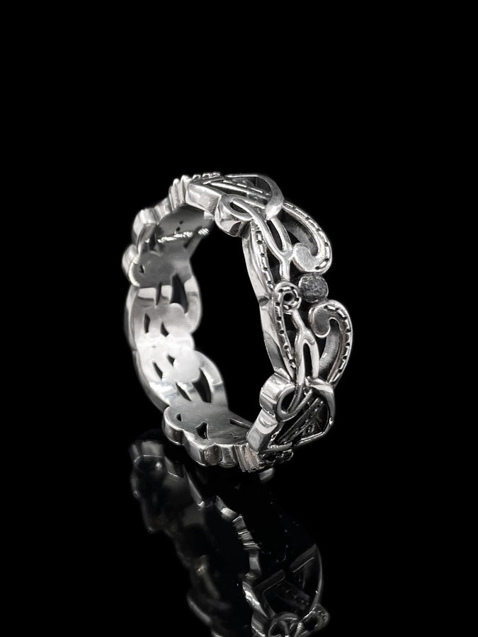 A studio shot of a matching two-piece sterling silver ring set on a black reflective surface. The standing ring is a signet style featuring an oval face with a raised Triskelion (triple spiral) motif. The ring lying flat is a wide band with an "openwork" or cut-out Celtic knot pattern. The silver is highly polished on the raised surfaces, contrasting with the dark shadows of the open areas.