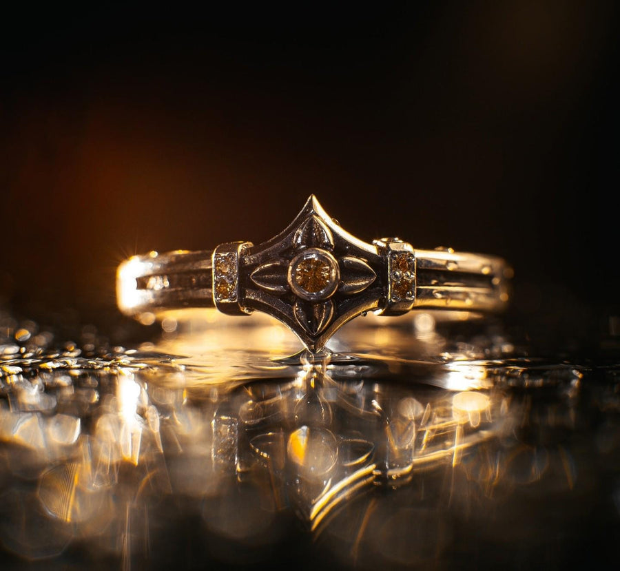 A macro photograph of a sterling silver ring with a distinct medieval silhouette. The centerpiece is a four-pointed "cross" or "star" shape holding a round, amber-hued gemstone (Citrine). The band is flanked by small, vertical bars set with tiny accent stones that sparkle in the light. The metal features a mix of high-polish highlights and dark, oxidized recesses, giving it an antique, artifact-like appearance. (etsy image id: 7488715953)