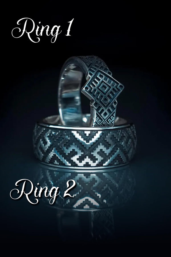A studio shot of a two-piece sterling silver ring set with a high-contrast black and silver finish. The standing ring features a square, diamond-shaped face created by stepped geometric lines. The lying ring is a wide band with a continuous "zig-zag" or "step" pattern running around the circumference. The design mimics the look of cross-stitch embroidery or pixelated ancient art rendered in metal.
