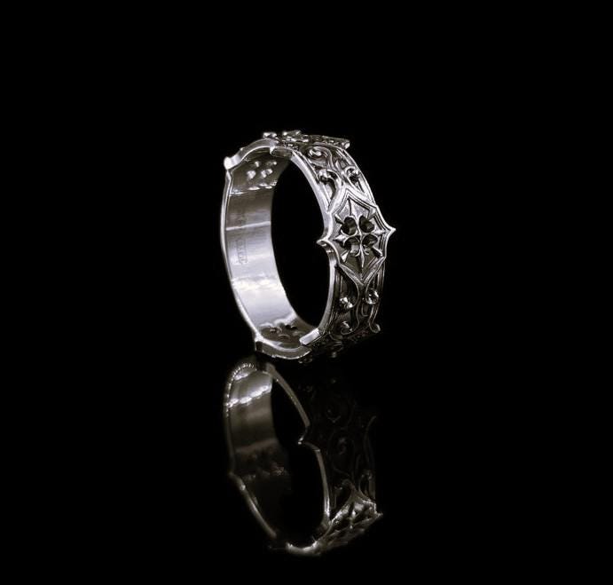 Handmade sterling silver band with an intricate gothic crown motif in the center, framed by swirling ornamental engravings. The deep relief and antique darkened finish evoke historic cathedral carvings. Ideal for customers seeking dark romantic jewelry, gothic accessories, medieval wedding rings, and meaningful silver bands with symbolic architecture-inspired designs. (etsy image id: 7423455351)