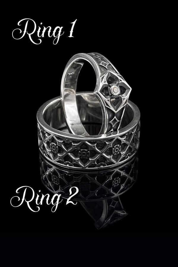 A professional studio photograph of a matching two-piece sterling silver wedding ring set. Both rings feature a prominent, raised Greek-style cross motif in the center, which holds a round, bezel-set white crystal. The interior of the cross arms has a fine, cross-hatched grid texture. Along the sides of the high-polished silver bands are recessed, four-lobed quatrefoil shapes. The rings are presented against a pitch-black background, making the p __etsy:8051335185