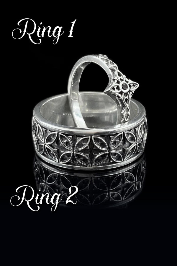 A professional studio photograph of a matching two-piece sterling silver wedding ring set. Both rings feature a prominent, raised Greek-style cross motif in the center, which holds a round, bezel-set white crystal. The interior of the cross arms has a fine, cross-hatched grid texture. Along the sides of the high-polished silver bands are recessed, four-lobed quatrefoil shapes. The rings are presented against a pitch-black background, making the p __etsy:8051335185
