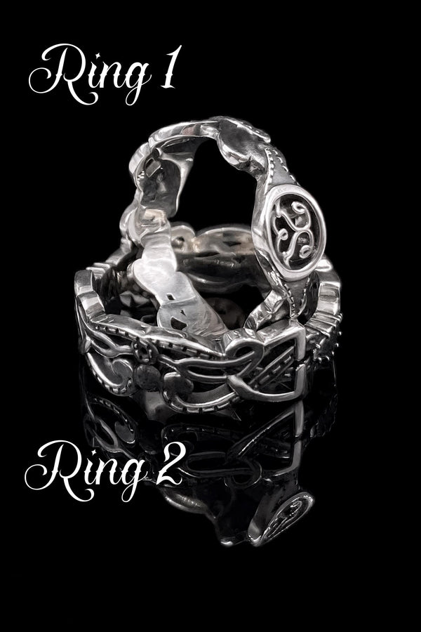 A studio shot of a matching two-piece sterling silver ring set on a black reflective surface. The standing ring is a signet style featuring an oval face with a raised Triskelion (triple spiral) motif. The ring lying flat is a wide band with an "openwork" or cut-out Celtic knot pattern. The silver is highly polished on the raised surfaces, contrasting with the dark shadows of the open areas.