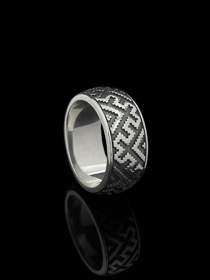 A studio shot of a two-piece sterling silver ring set with a high-contrast black and silver finish. The standing ring features a square, diamond-shaped face created by stepped geometric lines. The lying ring is a wide band with a continuous "zig-zag" or "step" pattern running around the circumference. The design mimics the look of cross-stitch embroidery or pixelated ancient art rendered in metal.