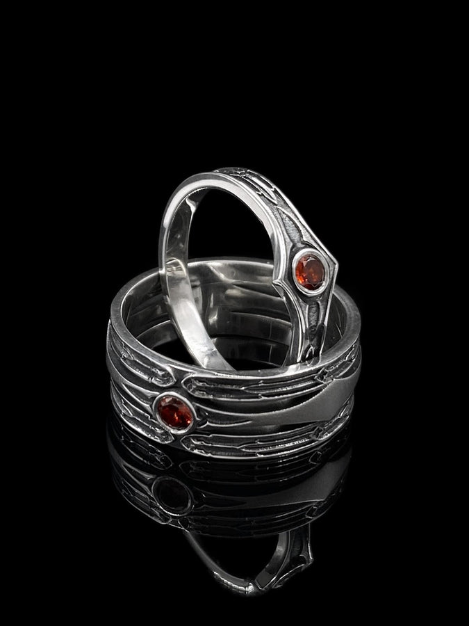 A cinematic close-up of a sterling silver ring with a distinct "V" shaped or "Lance Tip" contour. The focal point is a bezel-set, round gemstone with a deep amber-orange hue (Citrine or Madeira Citrine). The shoulders of the band feature horizontal grooves that taper toward the center, resembling the shaft of a spear or the fletching of an arrow. The metal is polished but features dark oxidation in the grooves for contrast. (etsy image id: 7489049399)