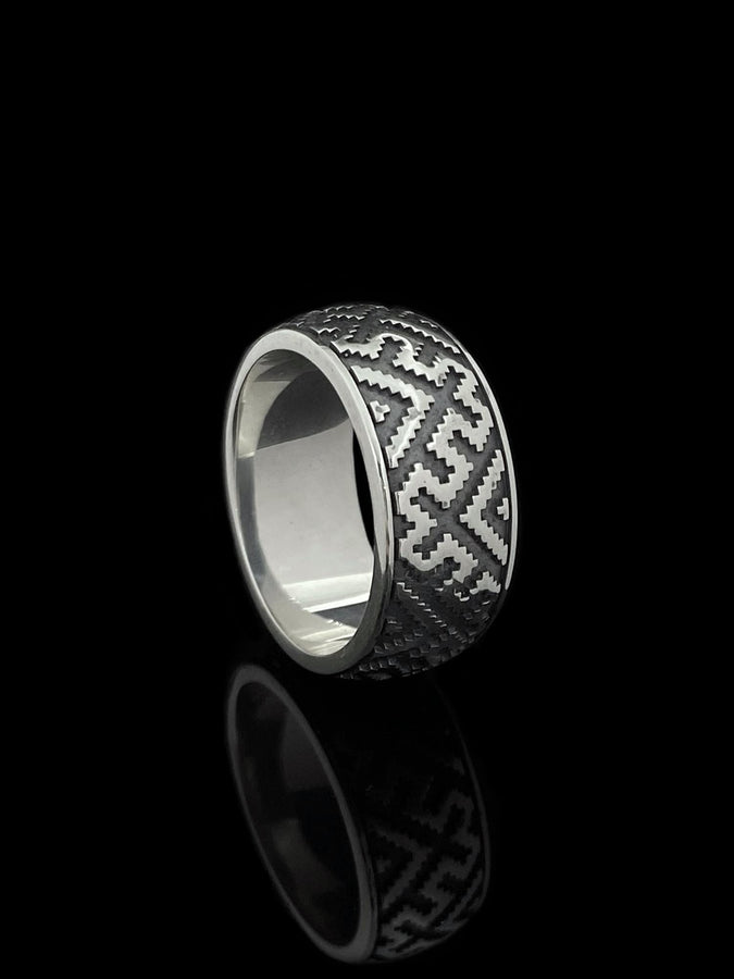 A detailed profile shot of a wide sterling silver ring featuring a repeating "step" or "zig-zag" pattern. The design wraps seamlessly around the entire band. The raised geometric lines are highly polished, catching the light, while the recessed areas are treated with a matte black oxidation. This creates a high-contrast, graphic look similar to a digital pixel pattern or traditional cross-stitch embroidery. (etsy image id: 7438608638)
