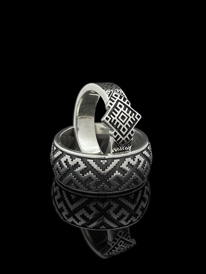 A detailed profile shot of a wide sterling silver ring featuring a repeating "step" or "zig-zag" pattern. The design wraps seamlessly around the entire band. The raised geometric lines are highly polished, catching the light, while the recessed areas are treated with a matte black oxidation. This creates a high-contrast, graphic look similar to a digital pixel pattern or traditional cross-stitch embroidery. (etsy image id: 7438608638)