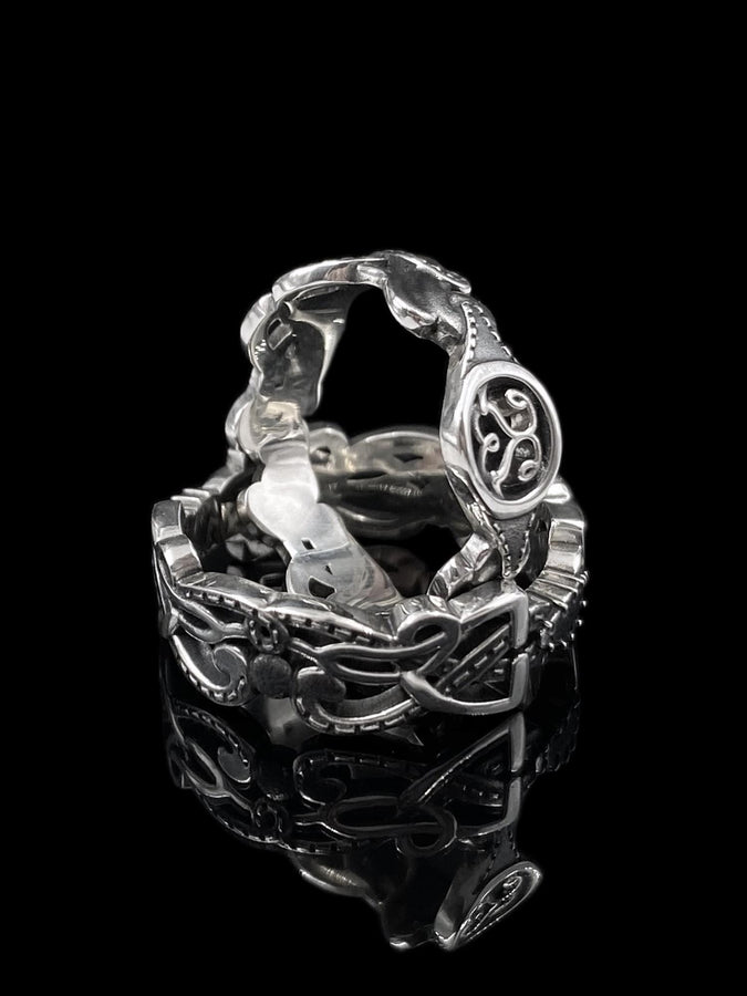 A cinematic close-up of a sterling silver ring lying on a reflective surface. The band features an "openwork" design, meaning the Celtic knot pattern is cut out, allowing light to pass through the loops. The silver strands weave over and under in a continuous infinity motif. The background is dark, but the ring is illuminated by a warm, golden mist. (etsy image id: 7442429936)