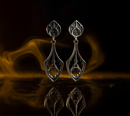 Witchy Earrings, Gothic Gift for Goth Girl, Handmade Vintage Earrings, Women Gift, A cinematic studio shot of a pair of dangle earrings standing on a dark, reflective surface. The design features a two-part construction: a top stud shaped like a pointed leaf or arch, and a larger bottom drop in a classic teardrop shape. Both sections are filled with openwork Gothic tracery—interlocking arches and trefoils. The silver is oxidized matte black in th (etsy image id: 7218819578)