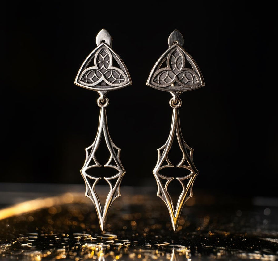 Embrace your dark beauty with our Gothic silver earrings. Unique design, premium silver, intricate details, and comfortable to wear.
A sharp studio shot of a pair of articulated silver earrings. The top stud is a soft triangle shape containing a raised "trefoil" or "trinity" knot pattern against a textured background. The bottom section is an elongated, openwork drop that tapers to a sharp point, resembling a Gothic spire or a (etsy image id: 7218877462)
