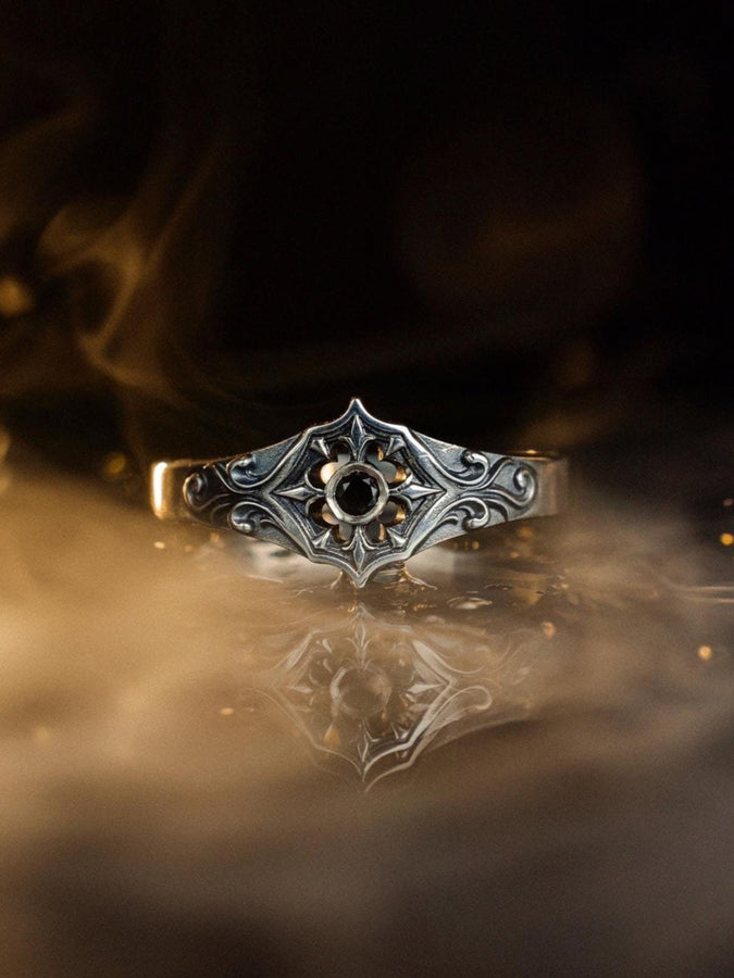 Close-up view of a gothic floral silver ring showcasing a detailed rose-inspired pattern and a polished black gemstone set in the middle. The intricate scrollwork surrounding the stone resembles cathedral tracery, giving the ring an old-world, medieval look. Perfect for engagement, weddings, anniversaries, or collectors of dark romantic jewelry and handcrafted artistic pieces. (etsy image id: 7243100328)
