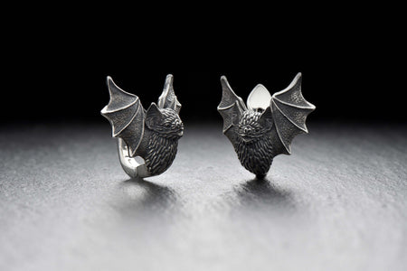mythic earrings	bat jewelry	gothic jewelry	bat lover	batman	bat gift	silver bat	bat garniture	bat lover gift	haloween gift	gothic	Fledermaus Ohrringe	boucles d'oreilles A high-resolution studio shot of a pair of plug bat earrings resting on a dark slate surface. Each earring features a detailed, three-dimensional sleeping bat folded securely within its webbed wings. The 925 sterling silver is heavily oxidized in the recesses to highlight the  (etsy image id: 7257833000)