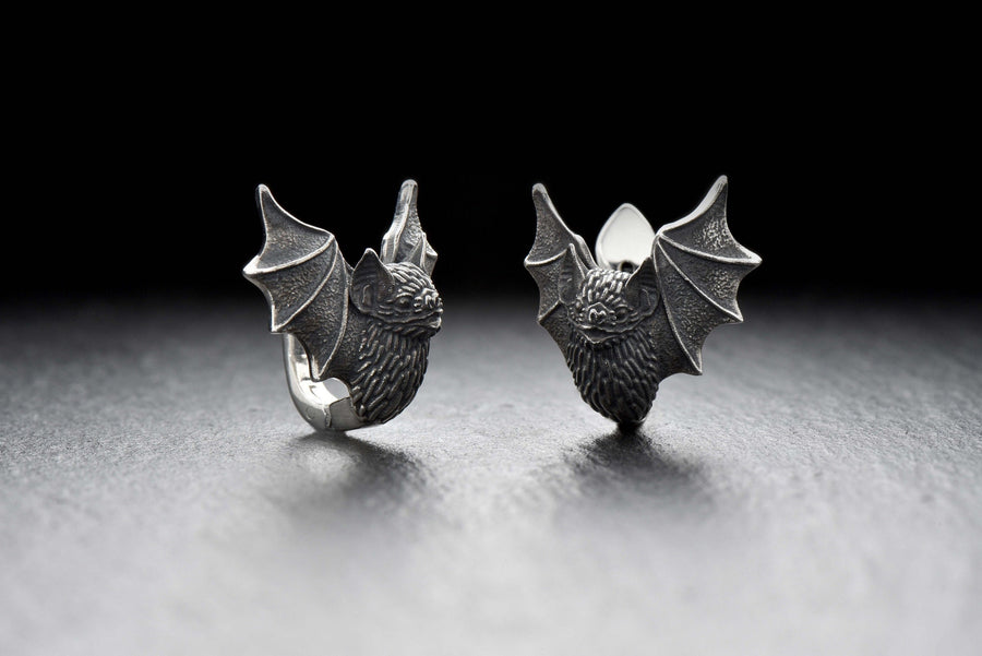 May include: A pair of silver earrings shaped like bats with detailed wings and faces. The hinged plug design allows them to sit securely and closely against the earlobe. Bathed in moody, low-key lighting, these gothic earrings evoke a mystical, nocturnal atmosphere perfect for a dark romance aesthetic. The beautifully detailed silver plug bat earrings capture the essence of vampirecore and whimsigoth fashion. (etsy image id: 5276595997)