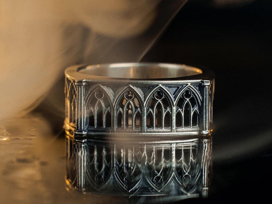 Defend your realm with this architectural fortress ring. Distinctive for its soft-square outer profile, this sterling silver band features a continuous cloister of Gothic arches anchored by robust corner buttresses. The geometric design mimics the stone ramparts of a medieval castle. Heavily oxidized to reveal the depth of the masonry, it is a symbol of unshakeable strength and structure. A bold statement for the guardian of history. (etsy image id: 7450412634)