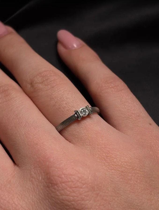 The photograph captures a slim Victorian silver ring with a gemstone framed by sculpted column motifs. Fine linear textures cover the band, giving it a classical, antique appeal. The gemstone sparkles softly, contrasting the darker oxidized grooves. This intricate design suits those who appreciate architectural jewelry, artistic detailing, and meaningful handmade engagement pieces. (etsy image id: 6976743880)