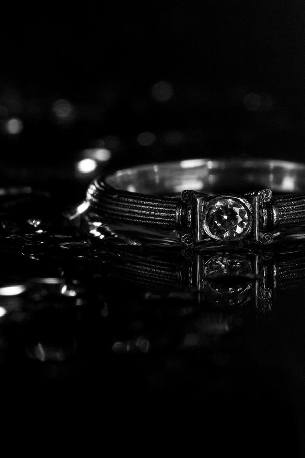 The photograph captures a slim Victorian silver ring with a gemstone framed by sculpted column motifs. Fine linear textures cover the band, giving it a classical, antique appeal. The gemstone sparkles softly, contrasting the darker oxidized grooves. This intricate design suits those who appreciate architectural jewelry, artistic detailing, and meaningful handmade engagement pieces. (etsy image id: 6976743880)