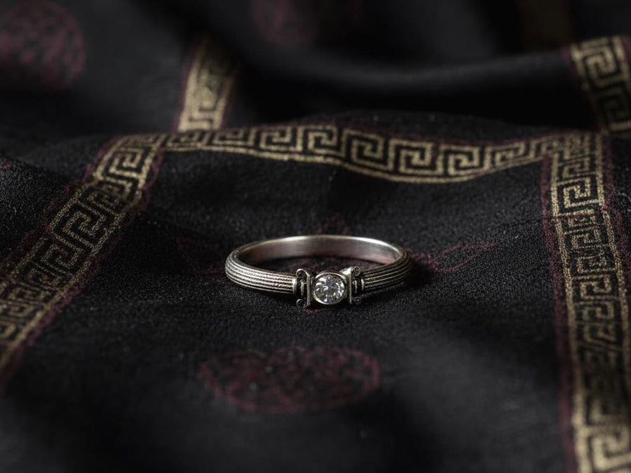 The photograph captures a slim Victorian silver ring with a gemstone framed by sculpted column motifs. Fine linear textures cover the band, giving it a classical, antique appeal. The gemstone sparkles softly, contrasting the darker oxidized grooves. This intricate design suits those who appreciate architectural jewelry, artistic detailing, and meaningful handmade engagement pieces. (etsy image id: 6976743880)
