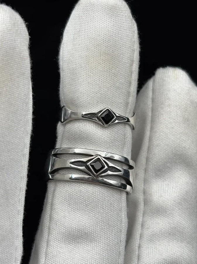 This Art Deco wedding ring set features a sterling silver engagement ring and matching band with bold geometric cutouts and a bright blue square gemstone. The clean lines, layered shapes, and sculptural silhouette create a modern yet vintage feel ideal for couples seeking unique, architecturally inspired bridal jewelry captured on a reflective surface for elegant presentation.