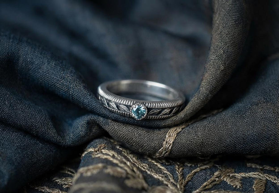A nature-inspired silver wedding ring featuring raised leaf motifs and a shimmering round gemstone set in the center. The Art Nouveau style is expressed through smooth curves and organic detailing along the band. Ideal for brides or grooms who appreciate delicate plant symbolism, handcrafted jewelry, and an elegant blend of vintage and contemporary design elements in their wedding set. (etsy image id: 6300134508)