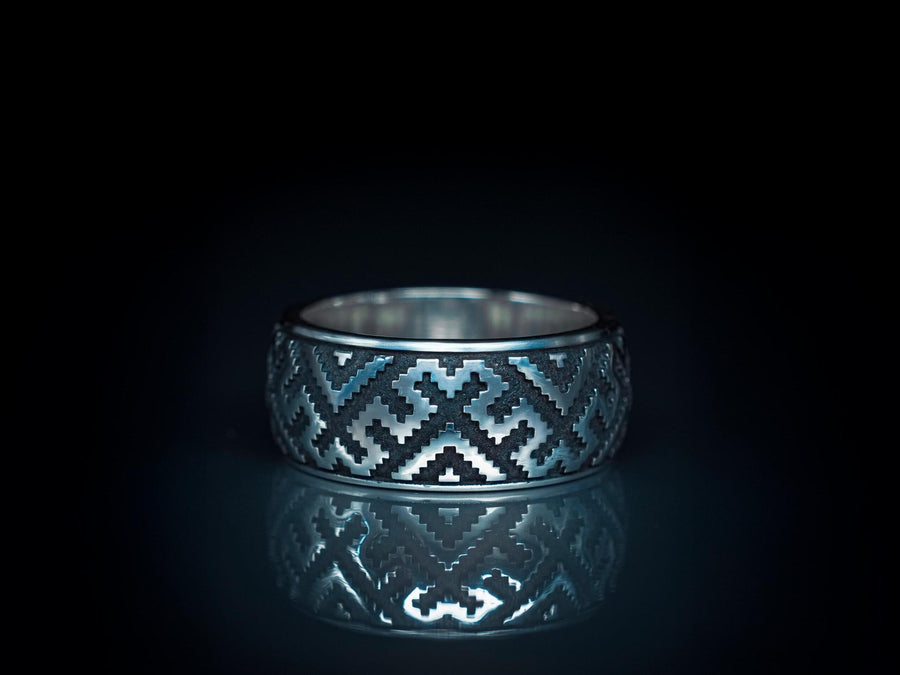A detailed profile shot of a wide sterling silver ring featuring a repeating "step" or "zig-zag" pattern. The design wraps seamlessly around the entire band. The raised geometric lines are highly polished, catching the light, while the recessed areas are treated with a matte black oxidation. This creates a high-contrast, graphic look similar to a digital pixel pattern or traditional cross-stitch embroidery. (etsy image id: 7438608638)