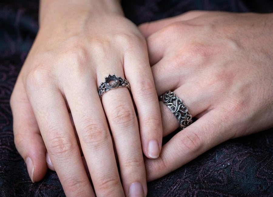 A high-contrast studio shot of a two-piece sterling silver ring set. The top ring features a raised, three-dimensional "crown" or "coronet" motif with small spheres on the tips. The bottom ring is a matching wide band. Both rings are covered in intricate, raised scrollwork or vine-like filigree. The silver is polished bright on the raised swirls, contrasting with the black oxidized background.