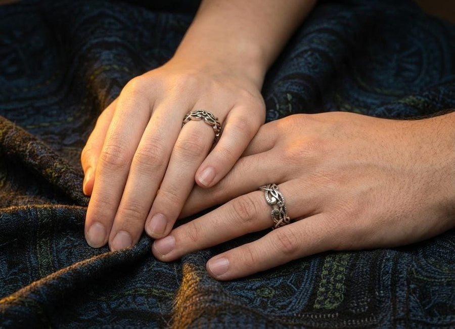 A cinematic close-up of a sterling silver ring lying on a reflective surface. The band features an "openwork" design, meaning the Celtic knot pattern is cut out, allowing light to pass through the loops. The silver strands weave over and under in a continuous infinity motif. The background is dark, but the ring is illuminated by a warm, golden mist. (etsy image id: 7442429936)