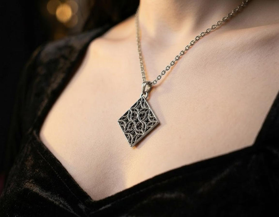 A detailed studio shot of a diamond-shaped (lozenge) sterling silver pendant hanging vertically. The design features intricate "curvilinear" Gothic tracery—four teardrop shapes meeting in the center to form a cross or quatrefoil. The raised lines are polished bright silver, while the negative space behind them is heavily oxidized to a matte black, creating a high-contrast architectural look. (etsy image id: 7494090955)
