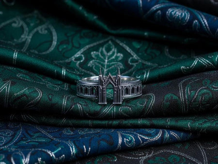 A cinematic studio shot of a sculptural sterling silver ring standing on a reflective surface. The design mimics the facade of a Gothic cathedral or castle gate. Two tall, pointed spires rise up on either side of a central archway. The band continues outwards with a colonnade of smaller arches. The silver features a beaded "cornice" detail along the edges and is heavily oxidized to emphasize the depth of the "stonework." (etsy image id: 7450300962)