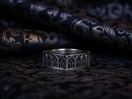 Defend your realm with this architectural fortress ring. Distinctive for its soft-square outer profile, this sterling silver band features a continuous cloister of Gothic arches anchored by robust corner buttresses. The geometric design mimics the stone ramparts of a medieval castle. Heavily oxidized to reveal the depth of the masonry, it is a symbol of unshakeable strength and structure. A bold statement for the guardian of history. (etsy image id: 7450412634)