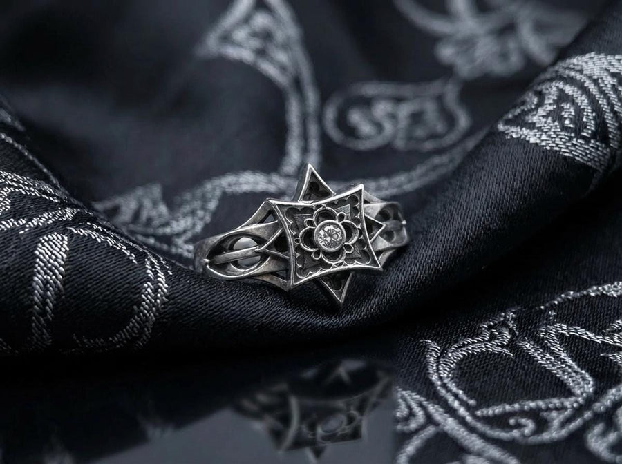 A detailed studio shot of a sterling silver ring held in a gloved hand. The focal point is a geometric "North Star" face—a square frame turned on its point, embellished with top and bottom spikes. Inside the frame is a floral quatrefoil pattern surrounding a round, bezel-set white gemstone (Diamond or CZ). The silver is polished on the raised lines and dark in the recesses. (etsy image id: 7452221522)