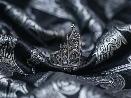 A clean studio shot of a sculptural sterling silver ring resting on a matte grey surface. The ring depicts a Gothic building facade with a tall, triangular central peak (gable) filled with geometric cross-shaped tracery. Flanking the center are lower pointed arches and vertical buttresses that wrap around the band. The silver is matte-finished with dark oxidation in the recesses to mimic stone shadows. (etsy image id: 7452370200)