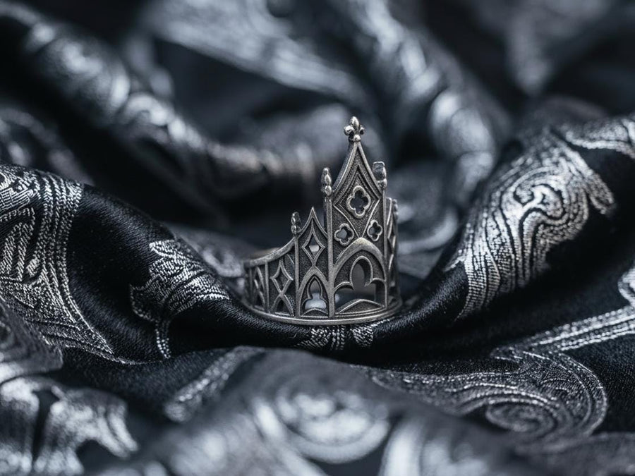 A clean studio shot of a sculptural sterling silver ring resting on a matte grey surface. The ring depicts a Gothic building facade with a tall, triangular central peak (gable) filled with geometric cross-shaped tracery. Flanking the center are lower pointed arches and vertical buttresses that wrap around the band. The silver is matte-finished with dark oxidation in the recesses to mimic stone shadows. (etsy image id: 7452370200)