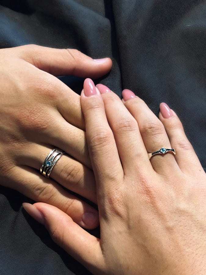 This Art Deco wedding ring set features a sterling silver engagement ring and matching band with bold geometric cutouts and a bright blue square gemstone. The clean lines, layered shapes, and sculptural silhouette create a modern yet vintage feel ideal for couples seeking unique, architecturally inspired bridal jewelry captured on a reflective surface for elegant presentation.