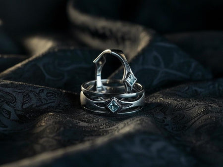 This Art Deco wedding ring set features a sterling silver engagement ring and matching band with bold geometric cutouts and a bright blue square gemstone. The clean lines, layered shapes, and sculptural silhouette create a modern yet vintage feel ideal for couples seeking unique, architecturally inspired bridal jewelry captured on a reflective surface for elegant presentation.