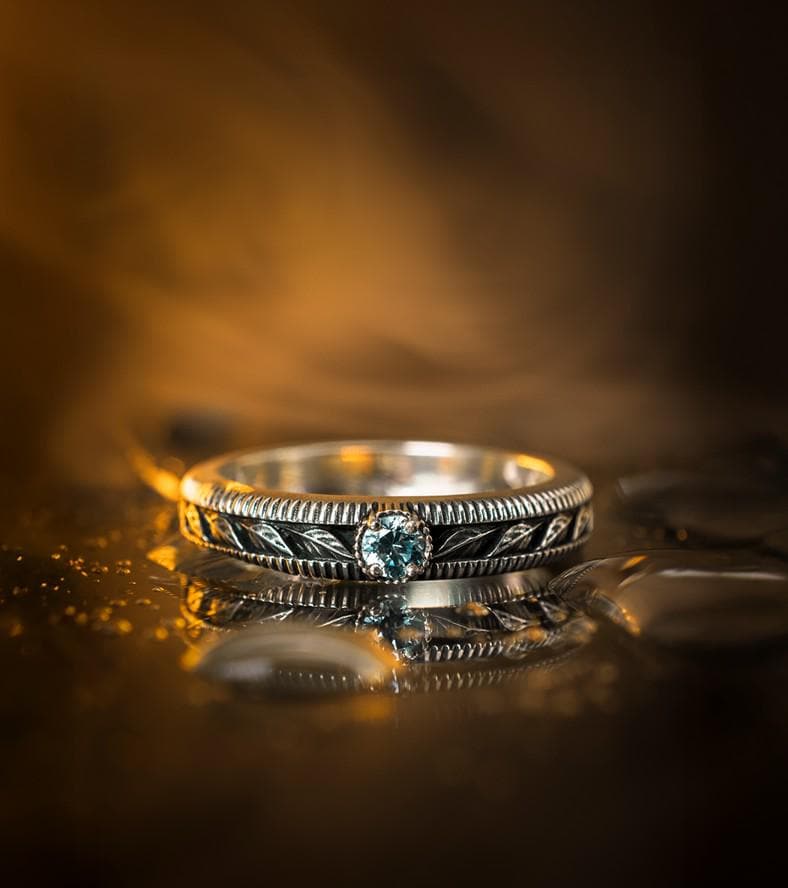 A nature-inspired silver wedding ring featuring raised leaf motifs and a shimmering round gemstone set in the center. The Art Nouveau style is expressed through smooth curves and organic detailing along the band. Ideal for brides or grooms who appreciate delicate plant symbolism, handcrafted jewelry, and an elegant blend of vintage and contemporary design elements in their wedding set. (etsy image id: 6300134508)