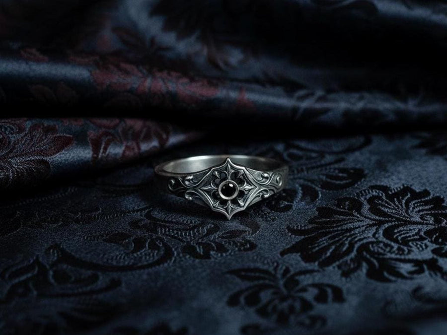 Close-up view of a gothic floral silver ring showcasing a detailed rose-inspired pattern and a polished black gemstone set in the middle. The intricate scrollwork surrounding the stone resembles cathedral tracery, giving the ring an old-world, medieval look. Perfect for engagement, weddings, anniversaries, or collectors of dark romantic jewelry and handcrafted artistic pieces. (etsy image id: 7243100328)