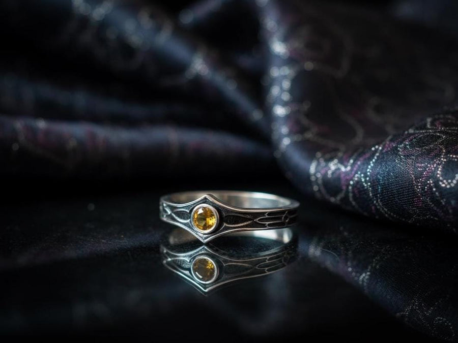 A cinematic close-up of a sterling silver ring with a distinct "V" shaped or "Lance Tip" contour. The focal point is a bezel-set, round gemstone with a deep amber-orange hue (Citrine or Madeira Citrine). The shoulders of the band feature horizontal grooves that taper toward the center, resembling the shaft of a spear or the fletching of an arrow. The metal is polished but features dark oxidation in the grooves for contrast. (etsy image id: 7489049399)