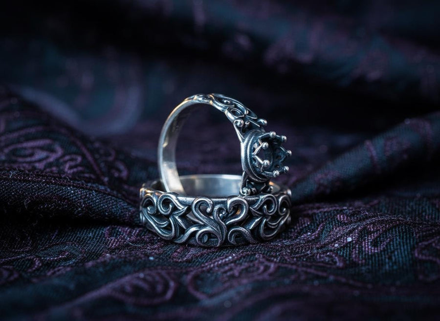 A high-contrast studio shot of a two-piece sterling silver ring set. The top ring features a raised, three-dimensional "crown" or "coronet" motif with small spheres on the tips. The bottom ring is a matching wide band. Both rings are covered in intricate, raised scrollwork or vine-like filigree. The silver is polished bright on the raised swirls, contrasting with the black oxidized background.
