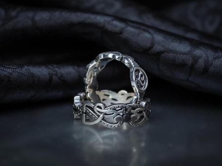 A studio shot of a matching two-piece sterling silver ring set on a black reflective surface. The standing ring is a signet style featuring an oval face with a raised Triskelion (triple spiral) motif. The ring lying flat is a wide band with an "openwork" or cut-out Celtic knot pattern. The silver is highly polished on the raised surfaces, contrasting with the dark shadows of the open areas.