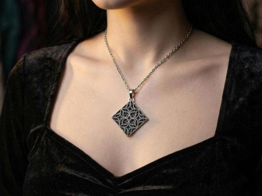 A detailed studio shot of a diamond-shaped (lozenge) sterling silver pendant hanging vertically. The design features intricate "curvilinear" Gothic tracery—four teardrop shapes meeting in the center to form a cross or quatrefoil. The raised lines are polished bright silver, while the negative space behind them is heavily oxidized to a matte black, creating a high-contrast architectural look. (etsy image id: 7494090955)