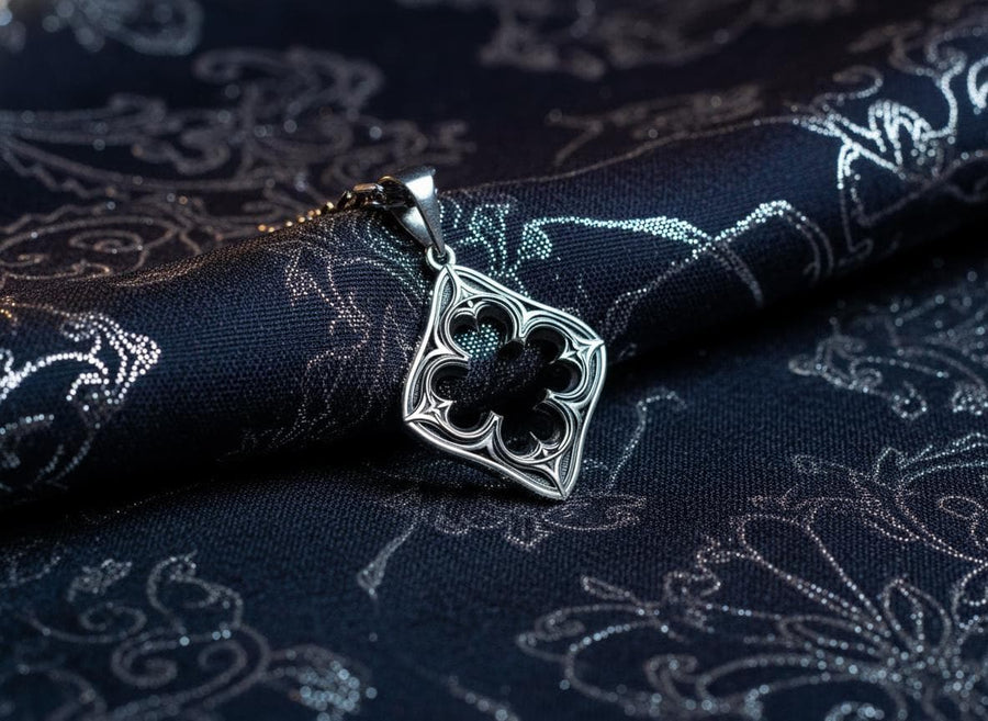 A cinematic studio shot of a diamond-shaped sterling silver pendant hanging against a smoky, amber-lit background. The design is "openwork," featuring a central cutout in the shape of a four-lobed quatrefoil. The silver frame mimics the stone mullions of a Gothic window, with pointed arches and sharp cusps. The metal is polished on the ridges and darkened on the sides to define the shape against the void. (etsy image id: 7496323581)