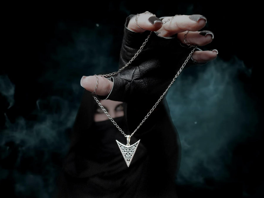 A detailed studio shot of an inverted triangle-shaped pendant hanging from a sturdy chain. The design features a "V" shape frame filled with complex, organic filigree. The inner pattern resembles branching roots, veins, or the "Flamboyant" style of late Gothic window tracery. The raised silver lines are polished bright, contrasting with the matte black oxidation in the negative spaces. (etsy image id: 7496362357)