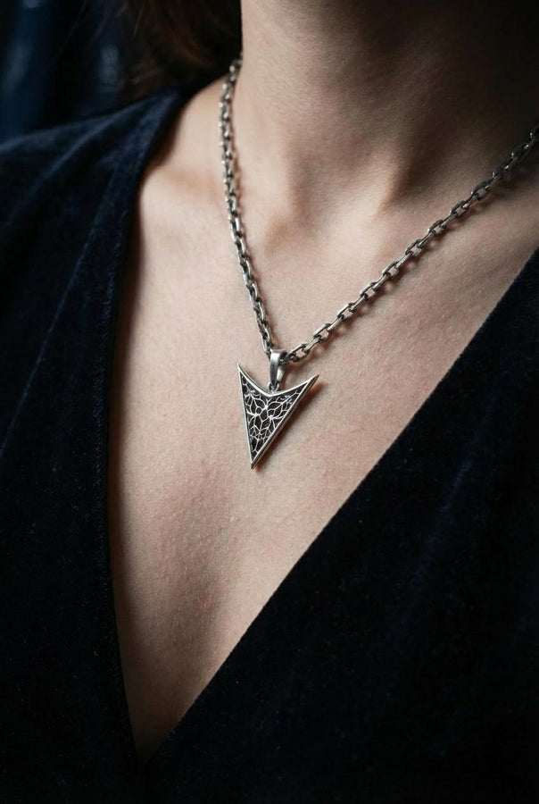 A detailed studio shot of an inverted triangle-shaped pendant hanging from a sturdy chain. The design features a "V" shape frame filled with complex, organic filigree. The inner pattern resembles branching roots, veins, or the "Flamboyant" style of late Gothic window tracery. The raised silver lines are polished bright, contrasting with the matte black oxidation in the negative spaces. (etsy image id: 7496362357)