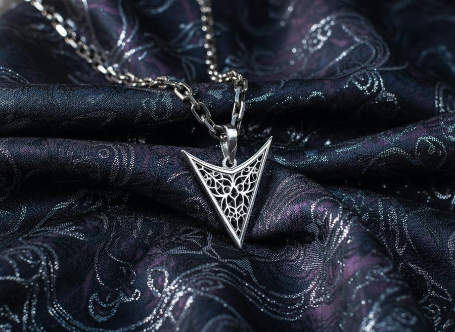 A detailed studio shot of an inverted triangle-shaped pendant hanging from a sturdy chain. The design features a "V" shape frame filled with complex, organic filigree. The inner pattern resembles branching roots, veins, or the "Flamboyant" style of late Gothic window tracery. The raised silver lines are polished bright, contrasting with the matte black oxidation in the negative spaces. (etsy image id: 7496362357)