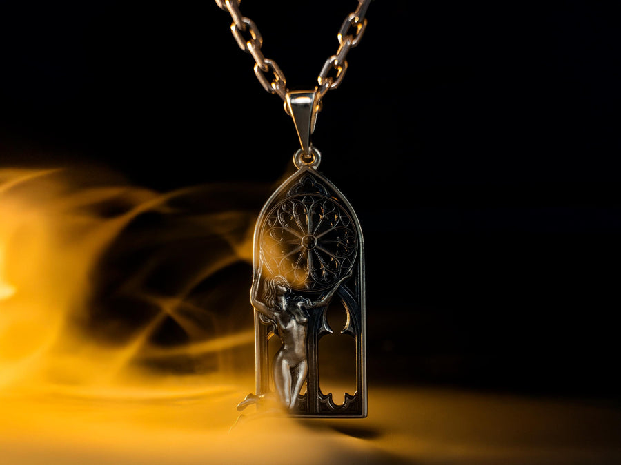 A cinematic studio shot of a tall, arched sterling silver pendant. The frame mimics a Gothic cathedral window. Inside the arch, a sculpted female figure (appearing nude) kneels or floats, reaching up to hold a large, circular "Rose Window" tracery wheel above her head. The silver is heavily oxidized, creating deep shadows behind the figure and the window spokes. (etsy image id: 7448666740)