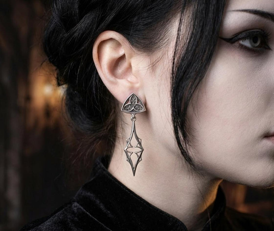 Embrace your dark beauty with our Gothic silver earrings. Unique design, premium silver, intricate details, and comfortable to wear.
A sharp studio shot of a pair of articulated silver earrings. The top stud is a soft triangle shape containing a raised "trefoil" or "trinity" knot pattern against a textured background. The bottom section is an elongated, openwork drop that tapers to a sharp point, resembling a Gothic spire or a (etsy image id: 7218877462)