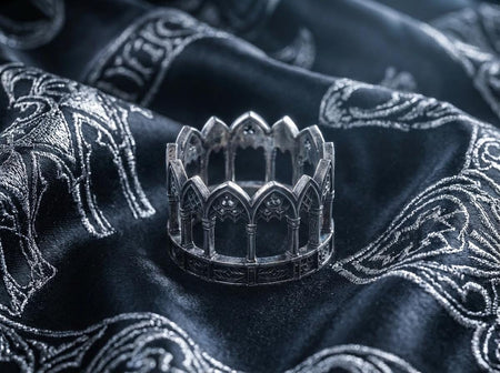 A cinematic studio shot of a sculptural sterling silver ring standing on a dark, textured fabric. The design forms a "crown" silhouette composed of a continuous row of Gothic pointed arches. Each arch is supported by vertical columns or pillars. Above the arches are circular "trefoil" or "quatrefoil" tracery details. The silver is heavily oxidized, with black recesses emphasizing the depth of the architectural relief (etsy image id: 7500079675)