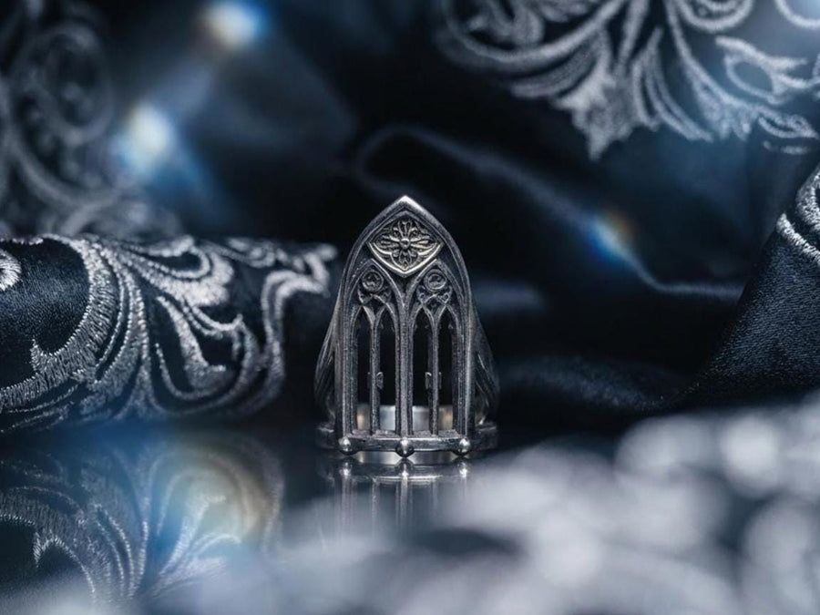 A clean studio shot of a tall, architectural sterling silver ring standing on a matte grey surface. The ring creates the silhouette of a Gothic "Lancet Window." It features three vertical openings separated by slender bars (mullions), topped by an intricate geometric tracery design within the pointed arch. The metal is matte silver with dark oxidation in the corners. (etsy image id: 7500328125)